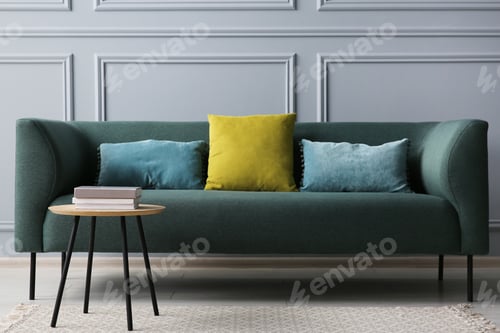 Preview: Stylish sofa with cushions and books on side table near grey wall