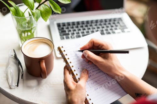 Preview: Female hands holding notebook and pen while making working notes by table