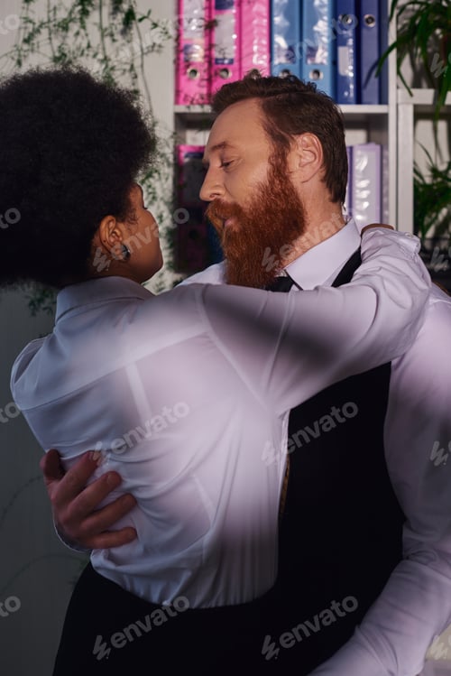 Preview: bearded businessman hugging young african american secretary, night romance in office