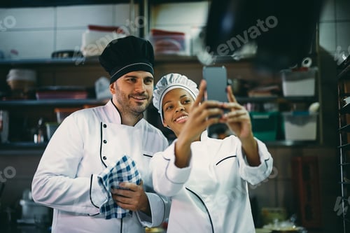 Preview: Happy chefs using smart phone and taking selfie in the kitchen.