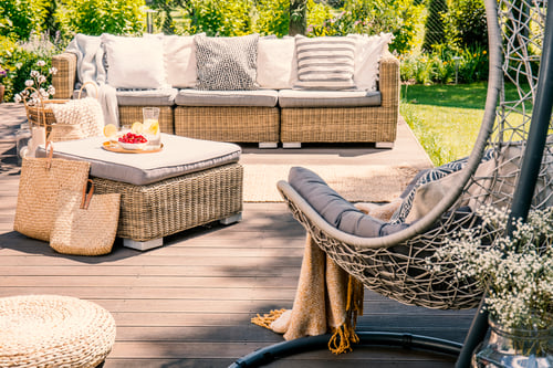 Pillows on rattan couch near table on patio with hanging chair i