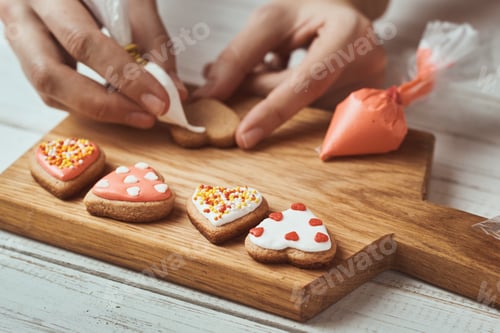 Preview: Decorating gingerbread cookies with icing. Woman hand decorate cookies in shape of heart, closeup