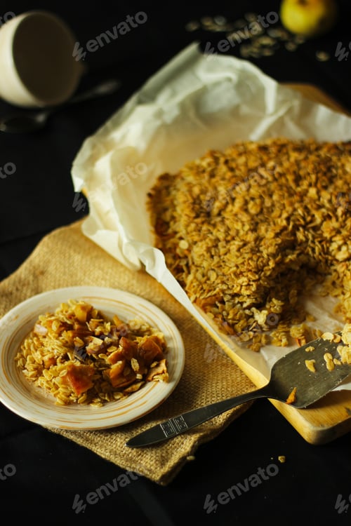 Preview: Portion of oatmeal granola baked with apples on a plate on the black-covered table