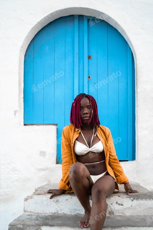 Preview: Stylish woman sitting outside house with blue door