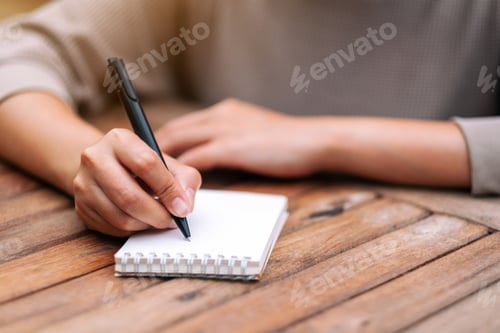 Preview: Closeup image of a woman writing on blank notebook on wooden table