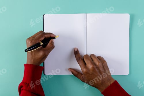 Preview: Hands of biracial man holding pen, writing in notebook with copy space on green background