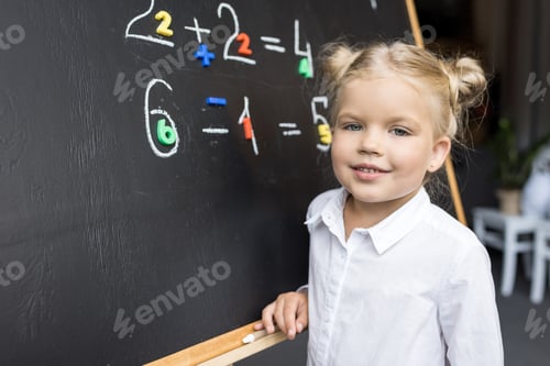 Preview: adorable little schoolgirl studying numbers and smiling at camera