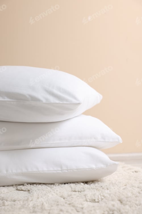 Preview: Stack of soft white pillows near beige wall indoors