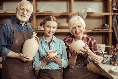 Preview: Granddaughter and grandparents standing and holding clay vase and bowls against wall with pottery