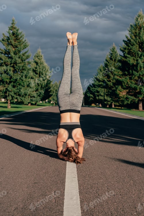 Preview: athletic woman performing Feathered Peacock yoga Pose while exercising on road in park