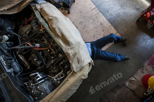 Preview: Mechanic lays on a trolley under a car in an auto repair shop
