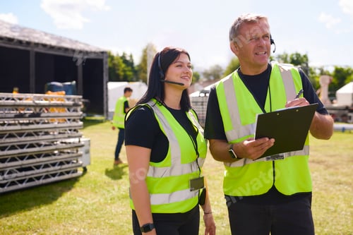 Preview: Male And Female Production Team With Headsets Setting Up Outdoor Stage For Music Festival Or Concert