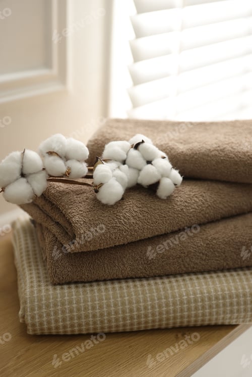 Preview: Stack of clean towels and cotton flowers on wooden table at home, closeup