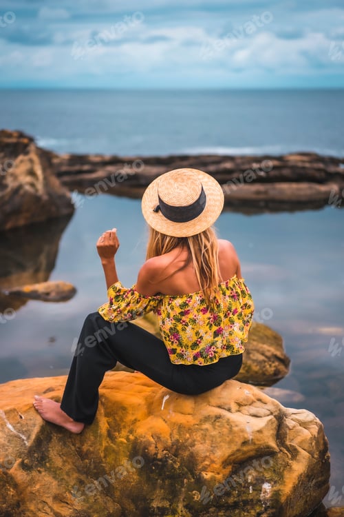 Preview: Girl in a floral shirt, black shorts and straw hat in a natural landscape by the sea