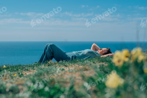 Preview: adult woman with a smile lies on the grass in the summer against the background of the sea, sky