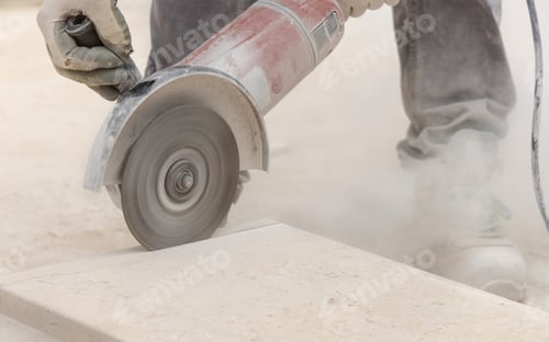 Preview: Craftsman in grey work clothes and helmet cutting marble piece during construction