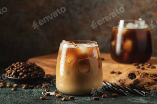 Preview: Ice coffee in a tall glass with cream poured over, ice cubes and beans on a dark concrete table.