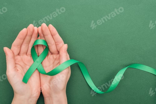 Preview: cropped view of woman holding green ribbon on green background with copy space