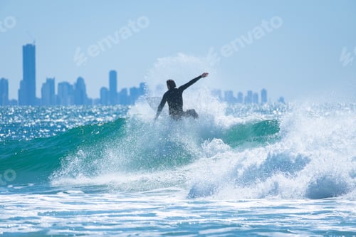 Preview: Young man surfing a wave in the blue sea with view of skyscrapers behind in Gold Coast, Australia