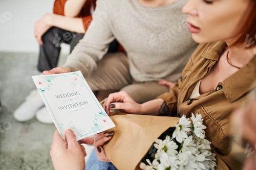 Preview: cropped view of shocked woman with flowers looking at wedding invitation near young gay couple