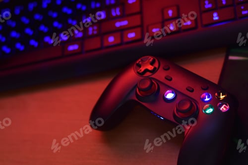 Preview: Modern gamepad lies with pc keyboard on table in dark playroom scene close up