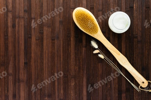 Preview: On a dark wooden table is an open jar of cream, a massage brush and dry flowers. The concept of cosm