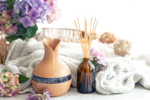 Preview: Aroma oil diffuser lamp, flowers and knitted element on a blurred background.