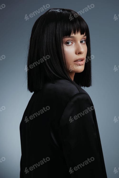 Preview: Beautiful woman with black hair wearing a black suit poses against a grey background, exuding