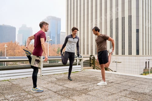 Preview: Three male athletes stretching legs in urban environment