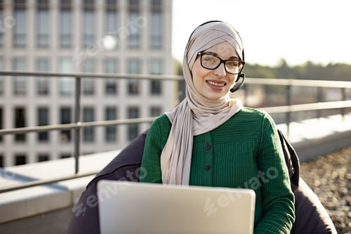 Preview: Arabian lady in headset staying with computer on terrace