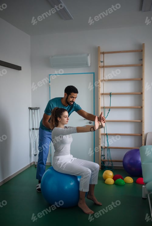 Preview: Young male physiotherapist exercising with young woman patient on ball in a physic room