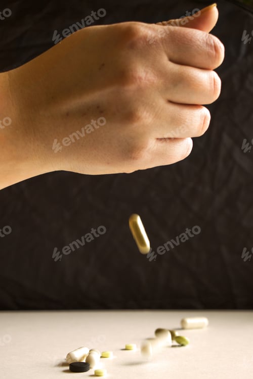 Preview: Vertical shot of a hand throwing pills on the table