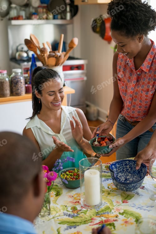 Preview: A group of women and men at a meal in a farmhouse kitchen.