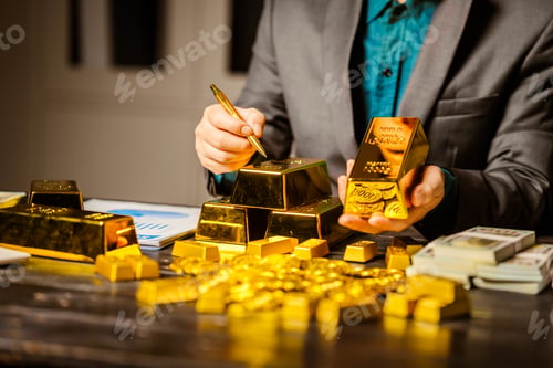 Preview: A businessman sits at his desk in a nighttime office, using a laptop to analyze gold bar prices