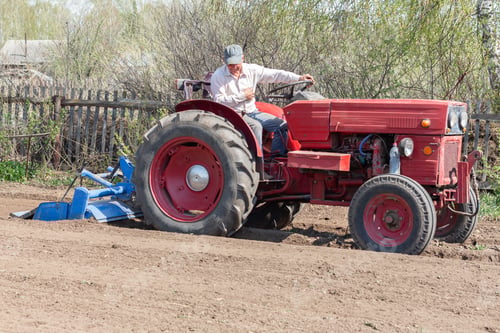 Preview: pensioner sitting on old tractor plows ground for planting seeds.