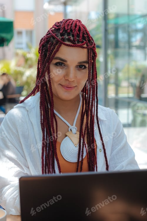 Preview: Beautiful diverse woman with dreadlocks working with laptop outdoor cafe
