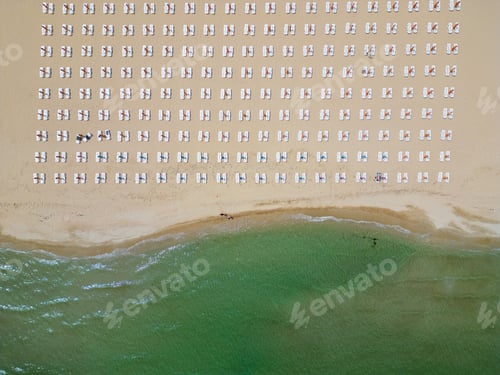 Preview: A sandy beach stretches along the seaside, adorned with empty sun loungers. Aerial view