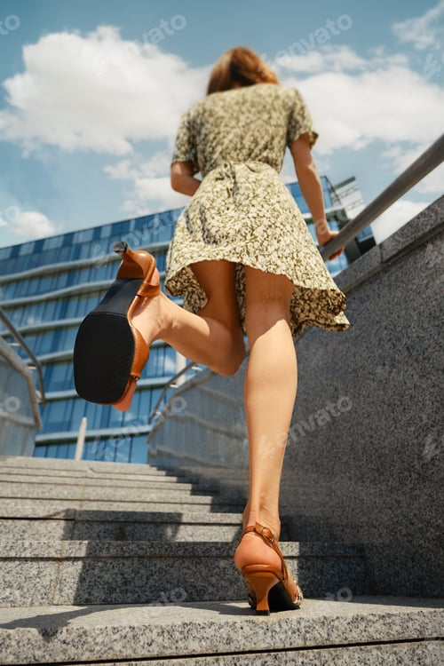 Preview: Rear view of a woman walking on stairs and showing the sole of her sandals