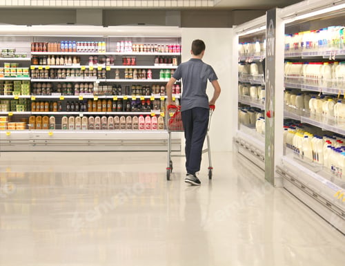 Preview: Young man doing grocery shopping pushing his shopping cart in the dairy section of the supermarket