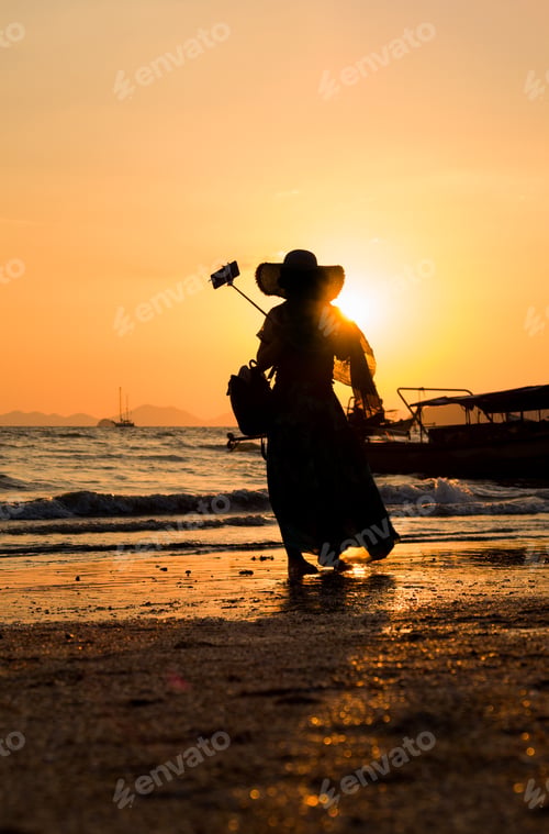 Preview: Asian woman taking selfies at the beach at sunset i