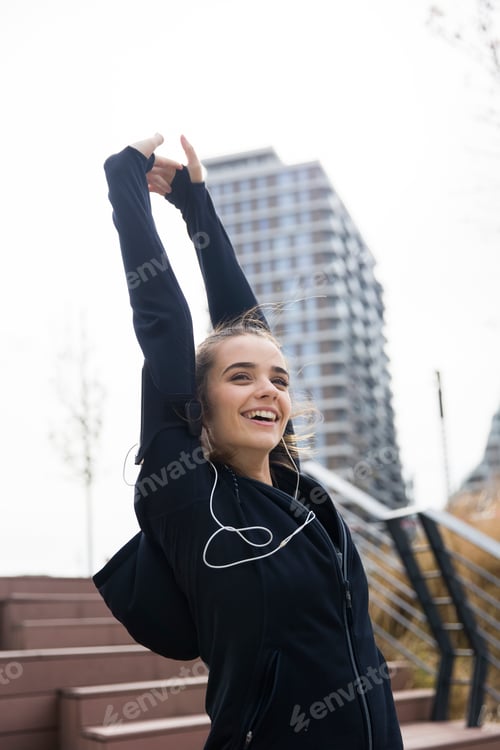 Preview: Female athlete stretching her arms while listening to music outdoors
