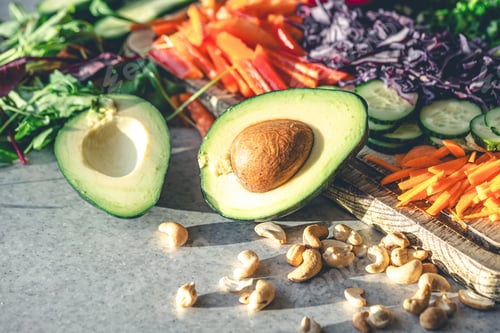 Preview: Avocado halves on the kitchen table with chopped fresh vegetables.