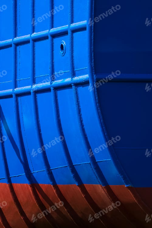 Preview: blue and red stern hull of large vessel with light and shadow on surface in vertical frame