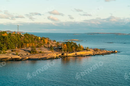 Preview: Aerial view of a serene coastline with a rocky shore, evergreen trees, and calm blue