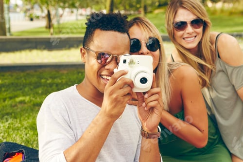 Preview: Young man and friends photographing with instant camera in park