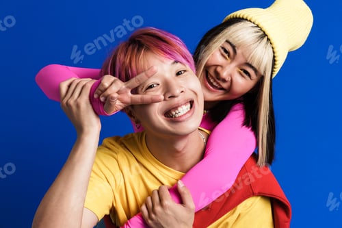 Preview: Asian couple with multicolored hair hugging while showing piece sign