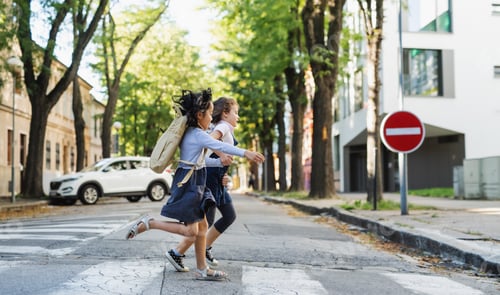 Preview: Side view of small school girls crossing street outdoors in town, running.