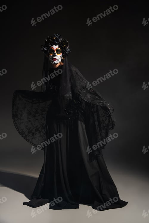 Preview: full length of woman in spooky santa muerte costume and catrina makeup on dark background