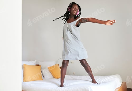 Preview: Woman wearing headphones is dancing on bed in bedroom