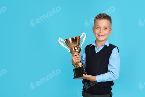 Preview: Happy boy in school uniform with golden winning cup on blue background. Space for text